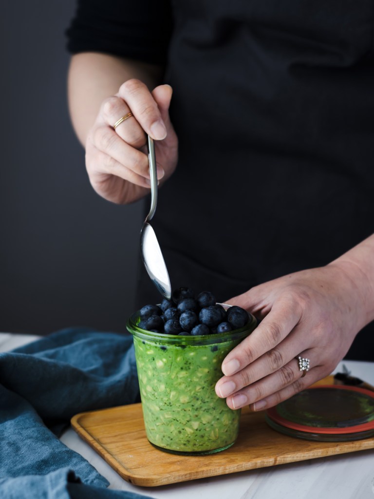 hand holding a spoon, digging into a glass jar with matcha overnight oats and blueberries 