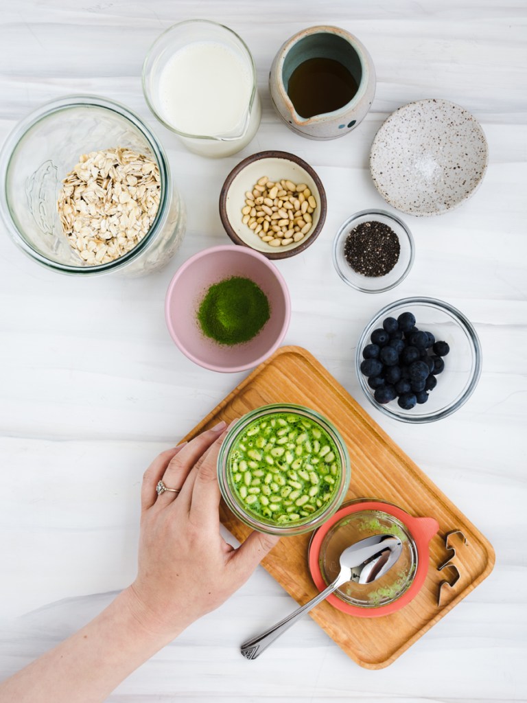 Ingredients for matcha overnight oats, hand holding a glass jar with matcha overnight oats