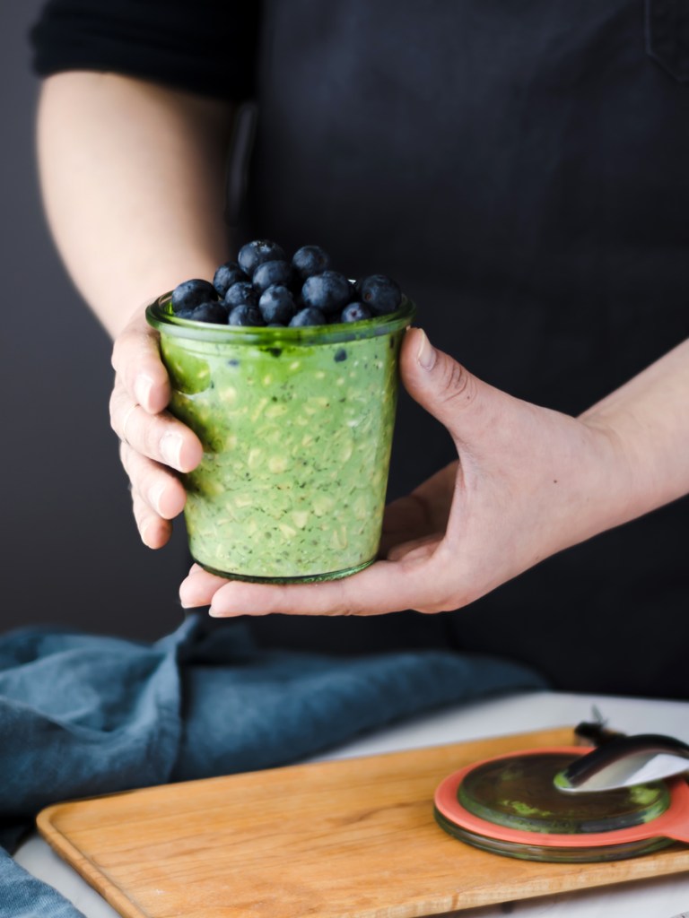 hands holding a glass jar with matcha overnight oats and blueberries 