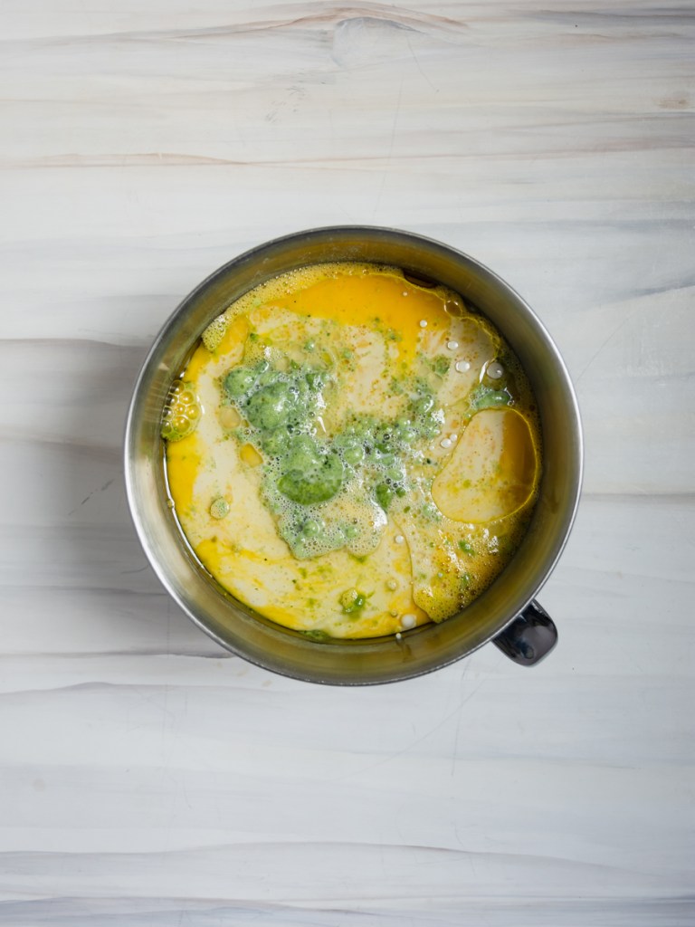 wet ingredients for matcha mochi cake: vegetable oil, milk, and eggs; stirred together inside a stainless steel stand mixer bowl on a marble-patterned background