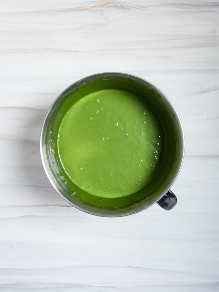 matcha mochi cake batter inside a stainless steel stand mixer bowl on a marble-patterned background